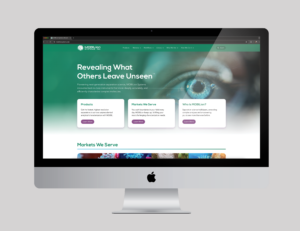 A desktop computer displays a website with a teal banner, the text “Revealing What Others Leave Unseen,” and three information cards about products, markets, and the company, featuring a close-up image of an eye in the background.