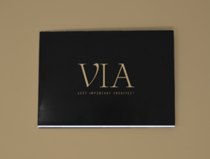 A black booklet with large gold text VIA and smaller text below reading VERY IMPORTANT ARCHITECT, placed on a beige surface—an elegant piece perfect for marketing or advertising purposes.