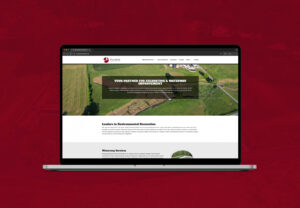 A laptop displaying a website with a banner reading Your Partner for Excavating & Waterway Improvement, set against an aerial view of fields on a dark red background—perfect imagery for marketing and advertising professionals.