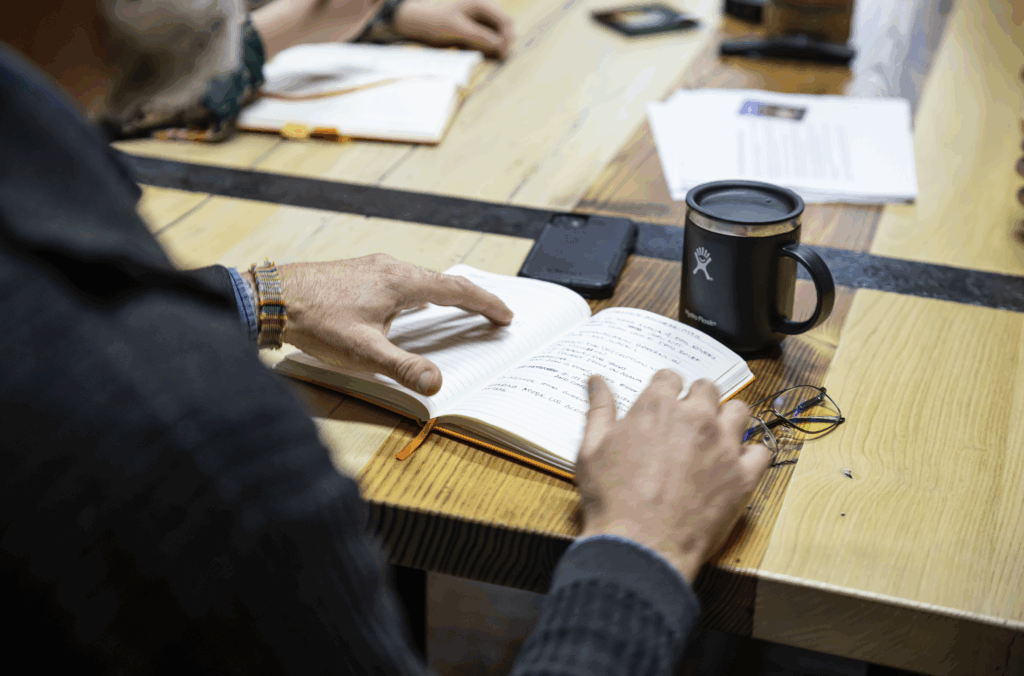 image of a persons hand touching a notebook which sits on a table with a tea mug on front