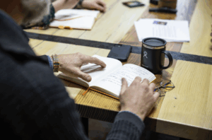 image of a persons hand touching a notebook which sits on a table with a tea mug on front