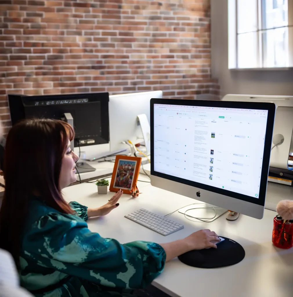 A woman sitting at a desk and using a computer in an office with a brick wall looks over a webpage.